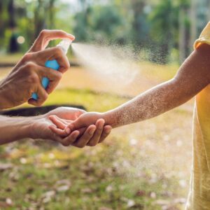 person spraying bug spray on a child's arm